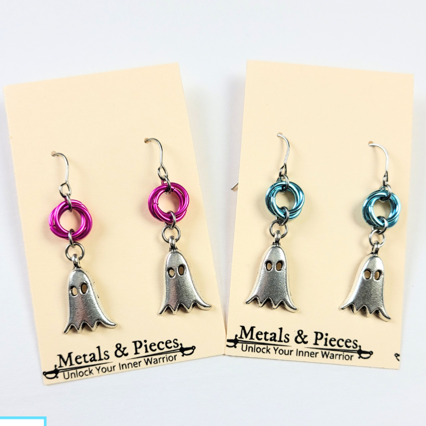 Summer Ghost Earrings in pink and blue color, made of metal and pieced together, displayed on a beige card with the brand name 'Metals & Pieces'.