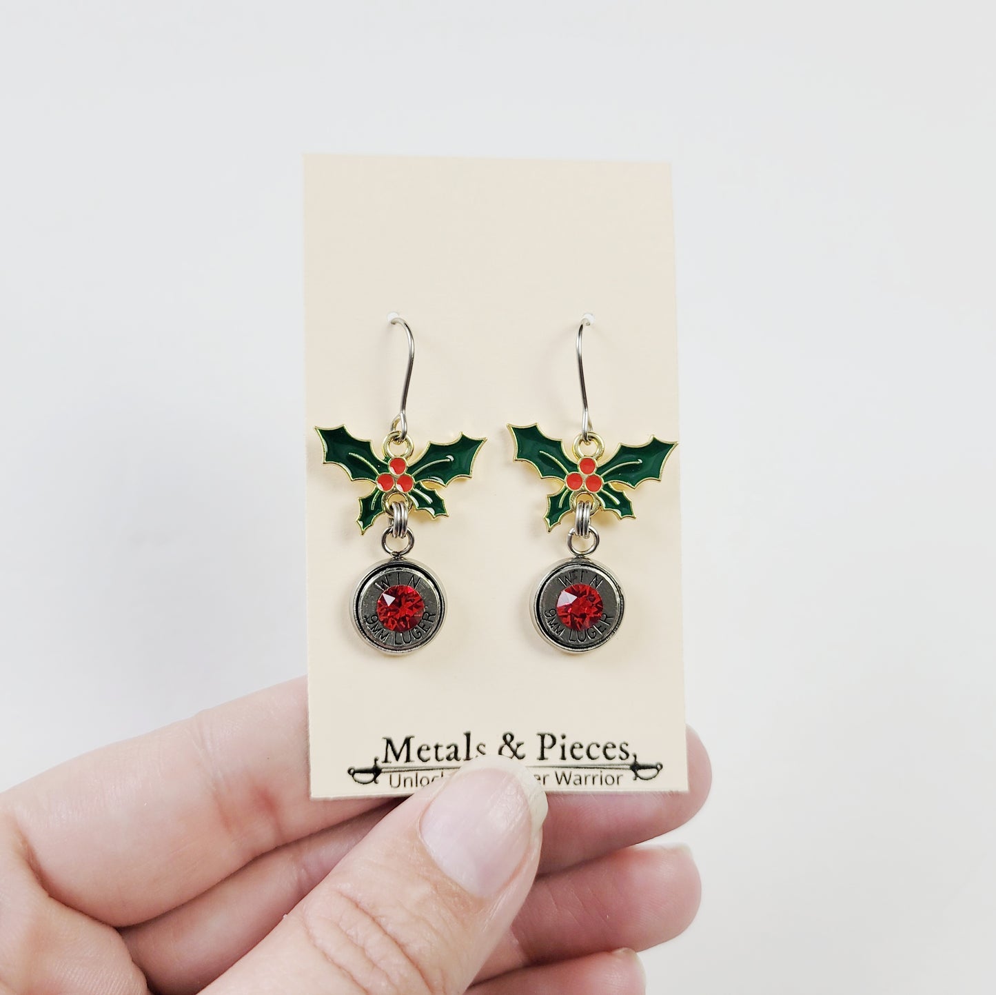 Gun-themed holiday earrings with enamel holly