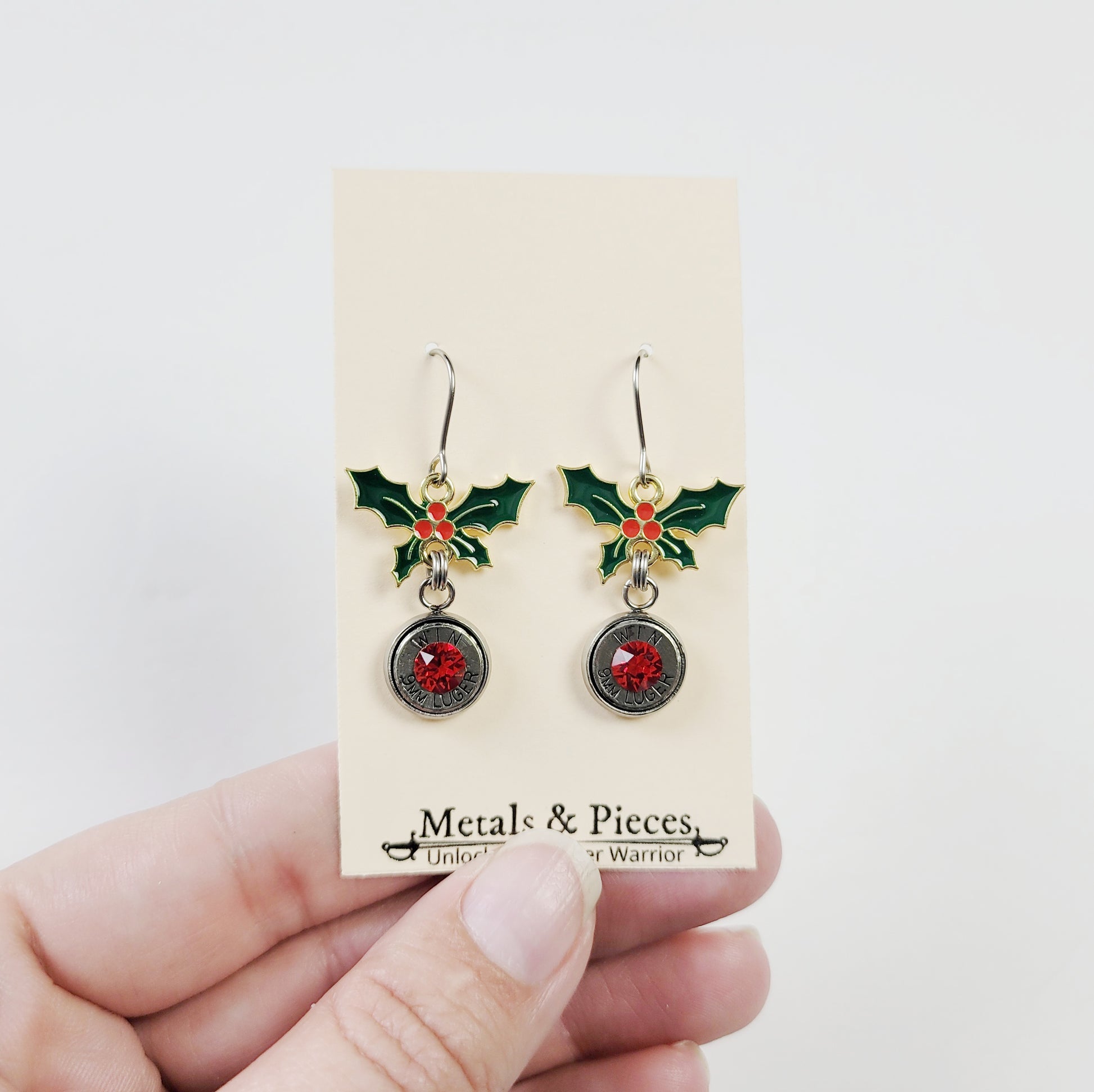 Gun-themed holiday earrings with enamel holly